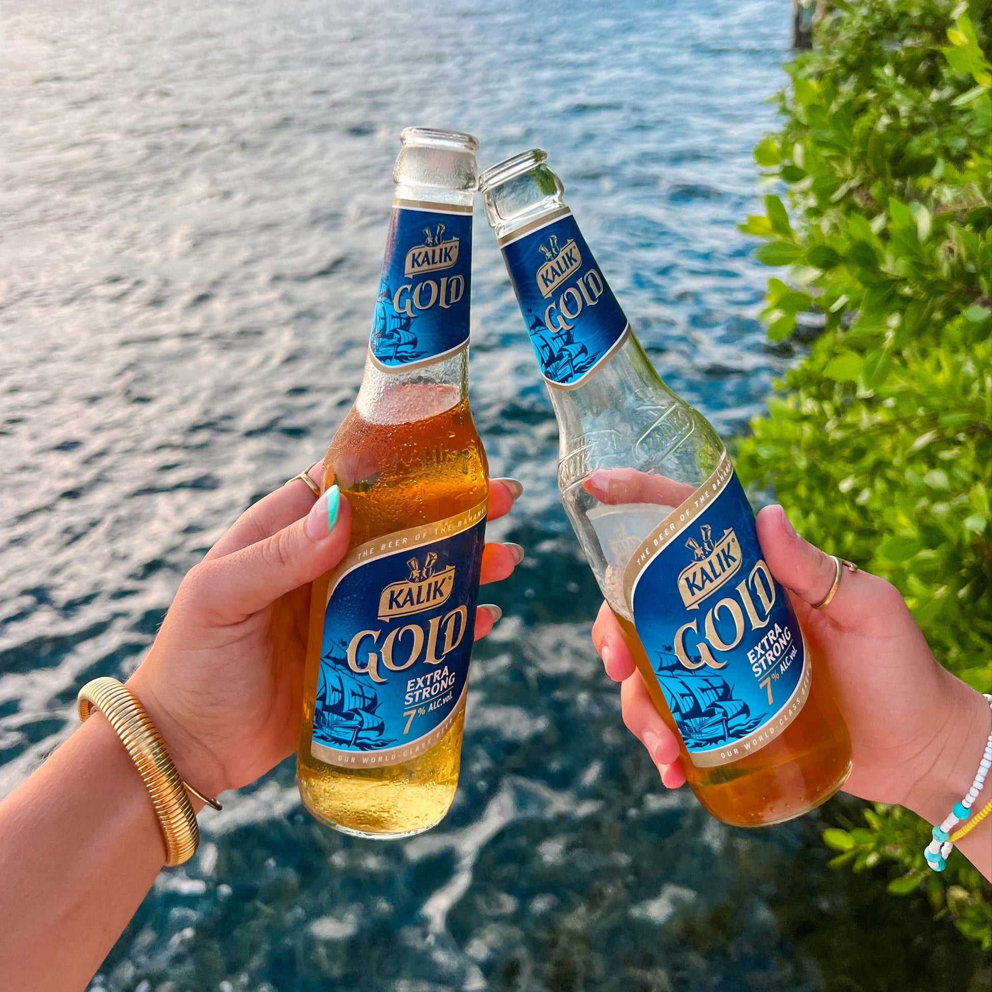 Two hands holding Kaldan Gold bottles by a waterfront