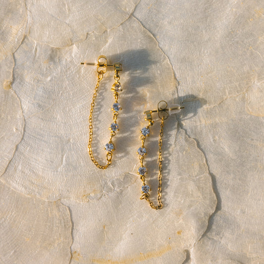 Gold chain earrings with small stones on a stone surface