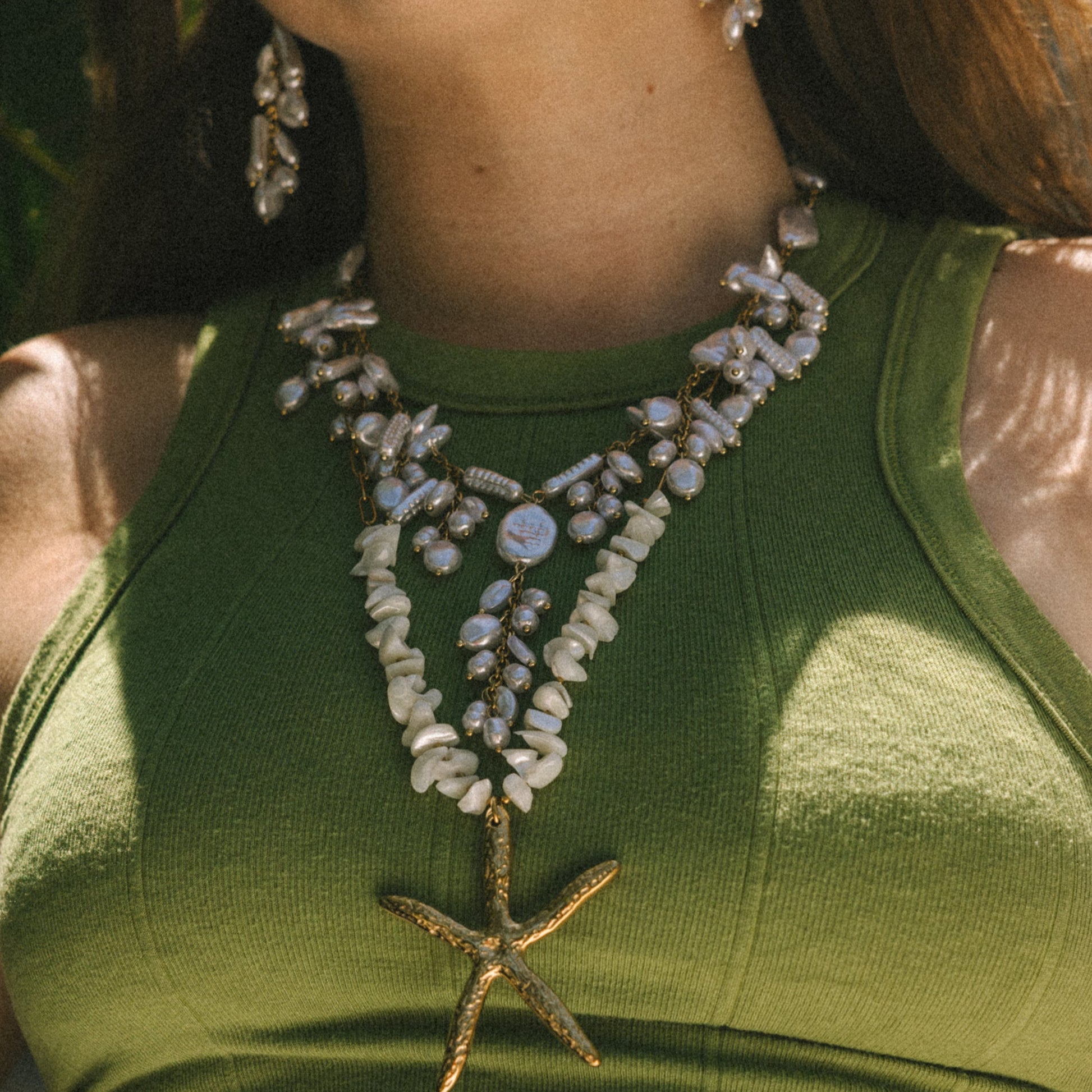 Person wearing a green top and a necklace with starfish pendant and blue stones.