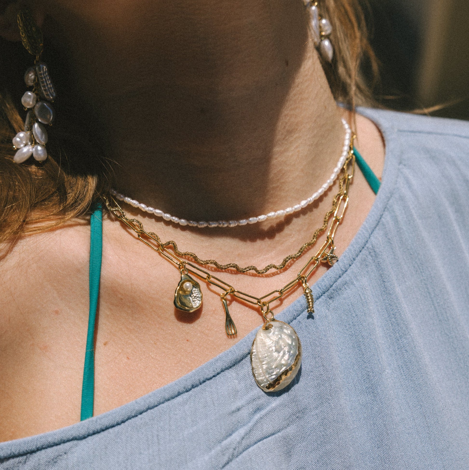 Close-up of a person wearing multiple necklaces with pendants on a blurred background