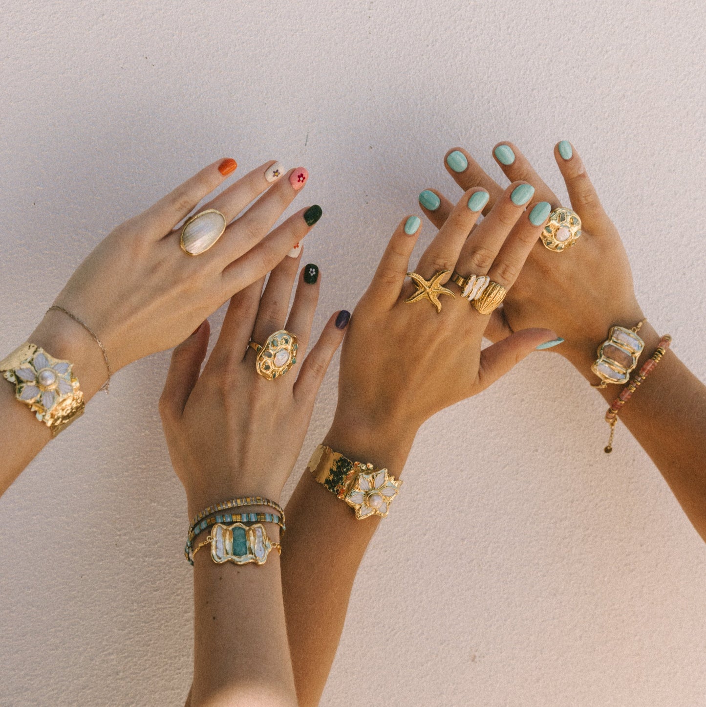Three hands with various rings and bracelets against a neutral background