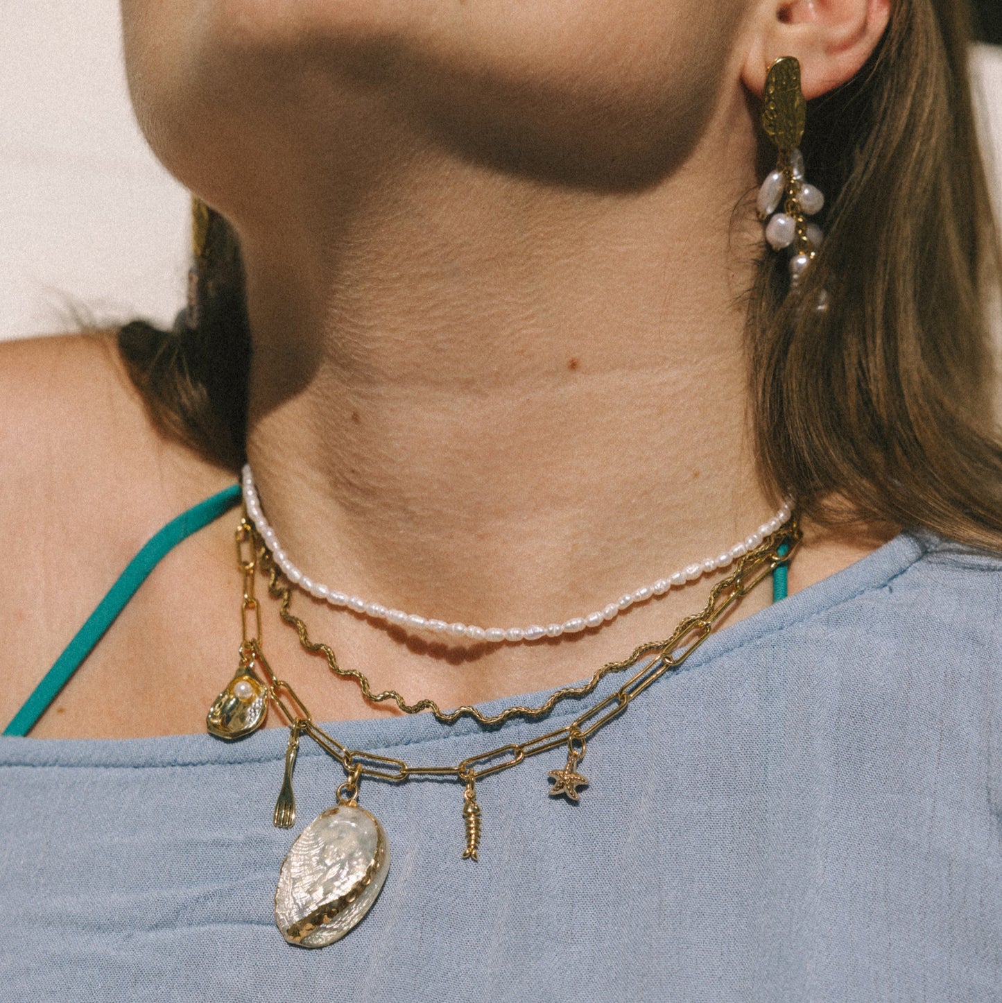Close-up of a woman wearing layered necklaces and earrings with a blurred background
