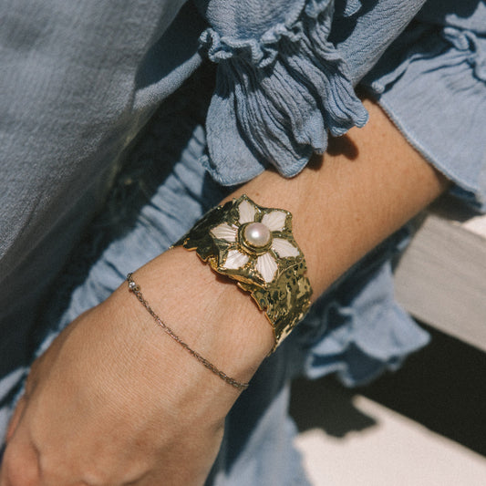 Close-up of a hand wearing a gold bracelet with floral design, set against a blurred background.