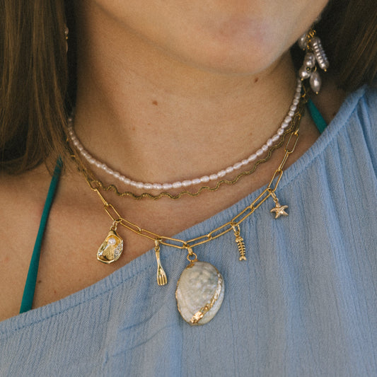 Close-up of a person wearing multiple necklaces with pendants on a blue top.