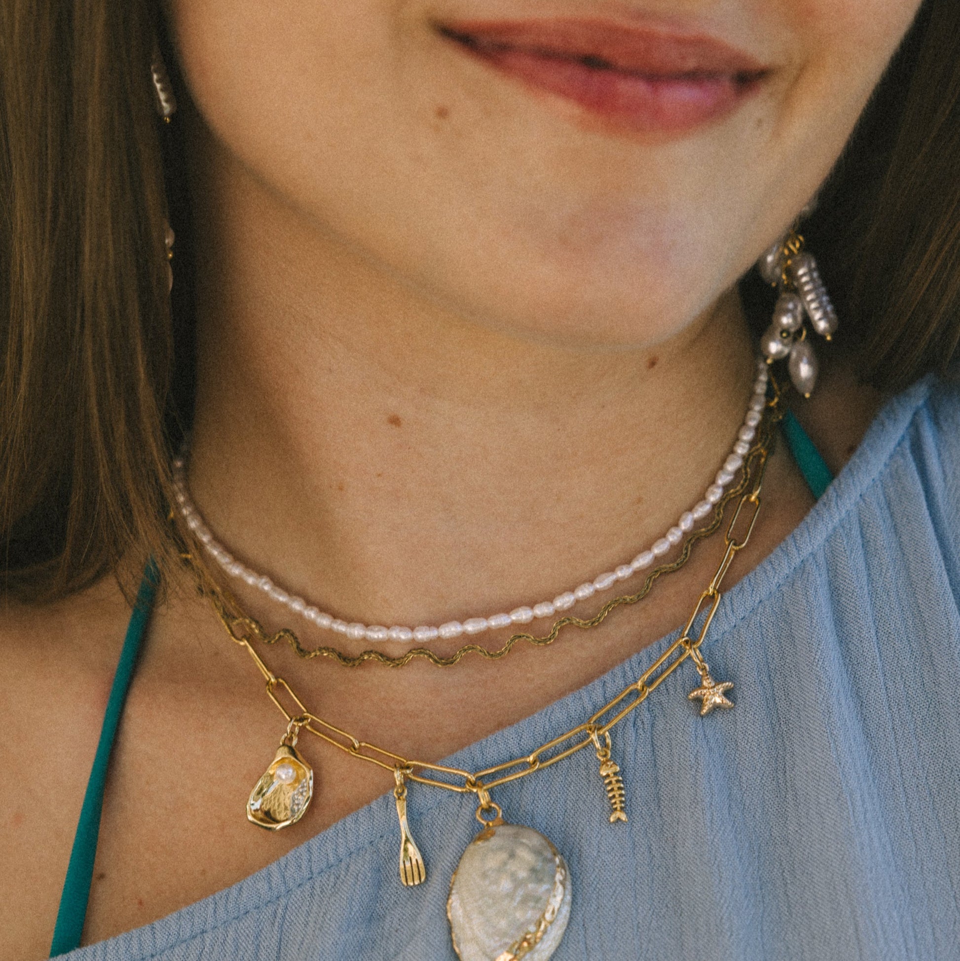 Close-up of a person wearing multiple necklaces with pendants on a blue top.