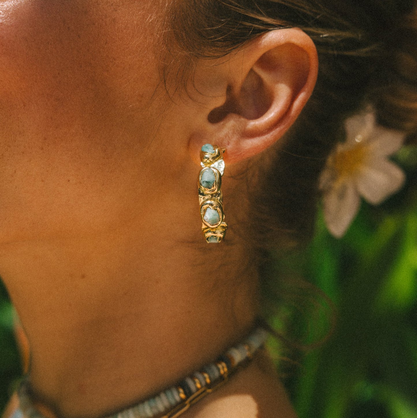 Close-up of a person wearing gold hoop earrings with turquoise stones, outdoors.