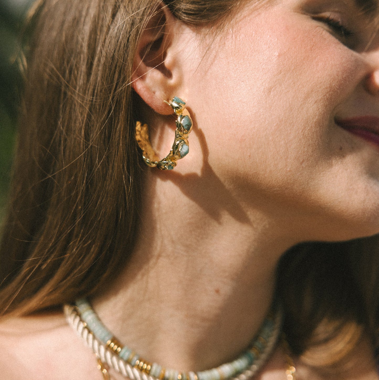 Close-up of a woman wearing gold hoop earrings and necklaces with a blurred background