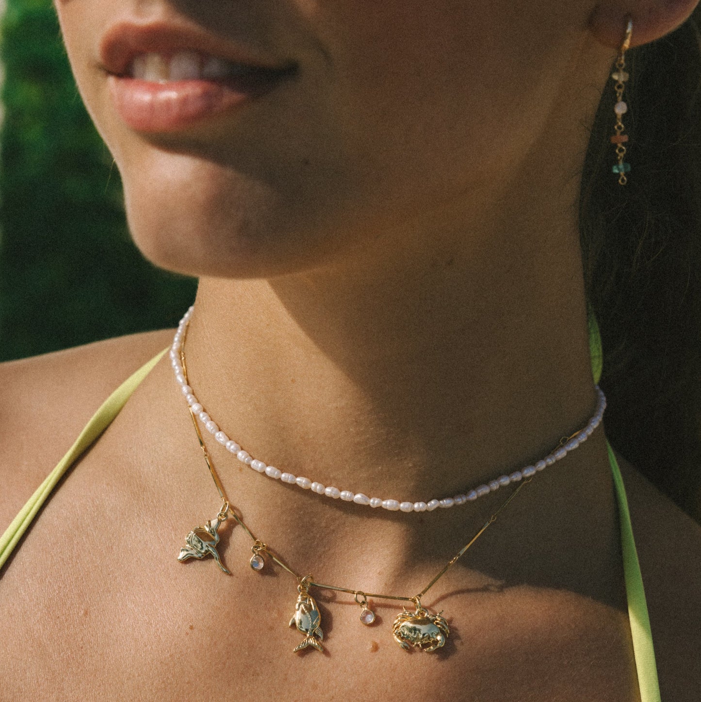 Close-up of a person wearing a necklace with pendant charms against a blurred natural background