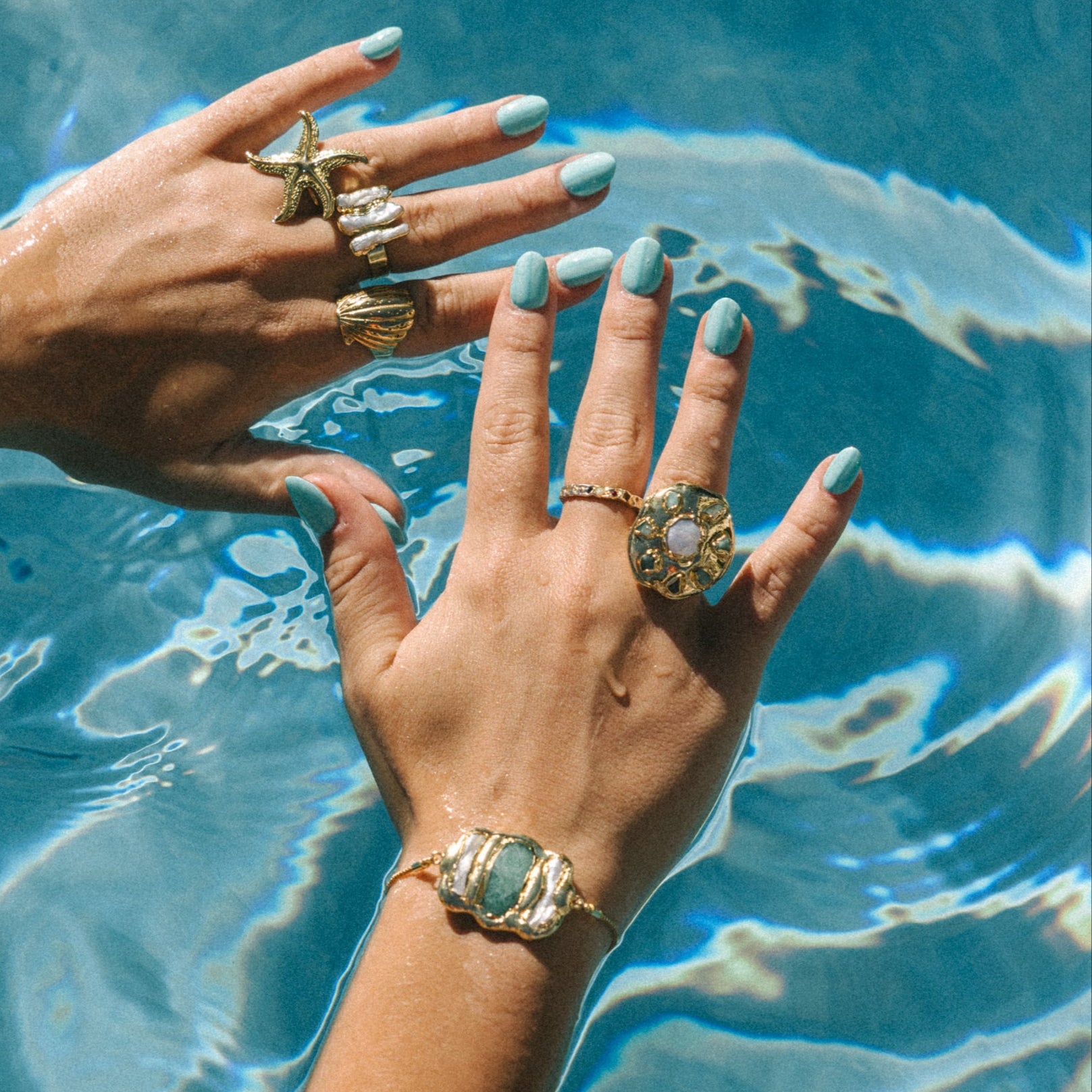 Hands with gold rings and bracelets against a blue water background