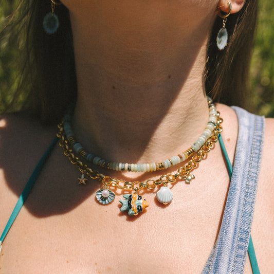 Close-up of a person wearing a gold necklace with charms against a blurred natural background