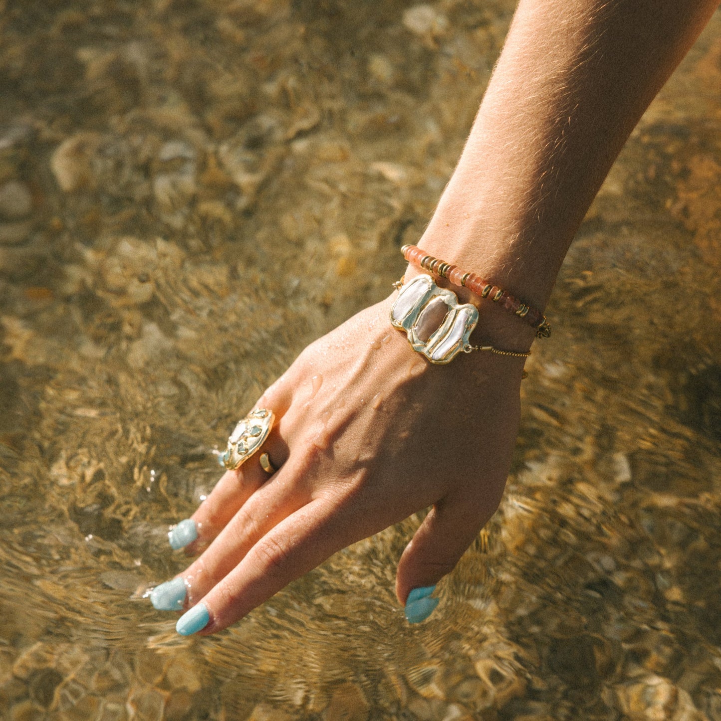 Hand with rings and bracelets touching clear water