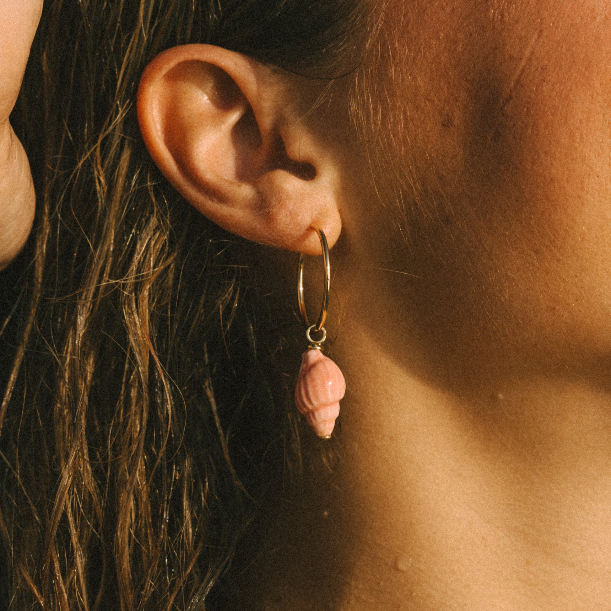 Close-up of an ear wearing a pink bead earring with a blurred background