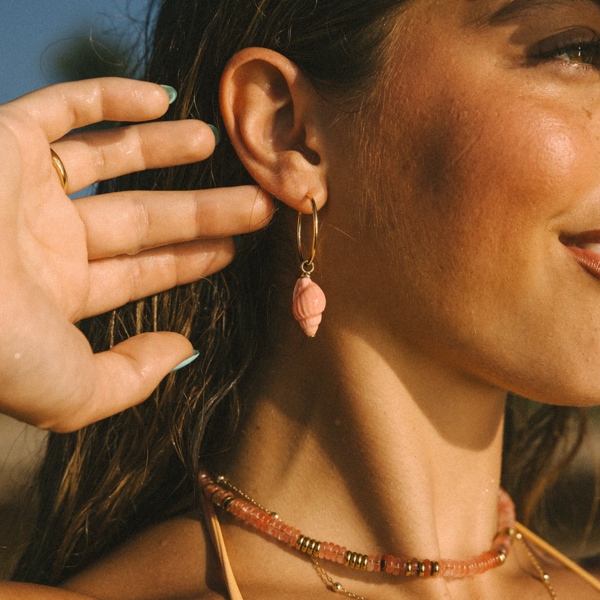 Close-up of a woman wearing a pink earring and gold necklaces.