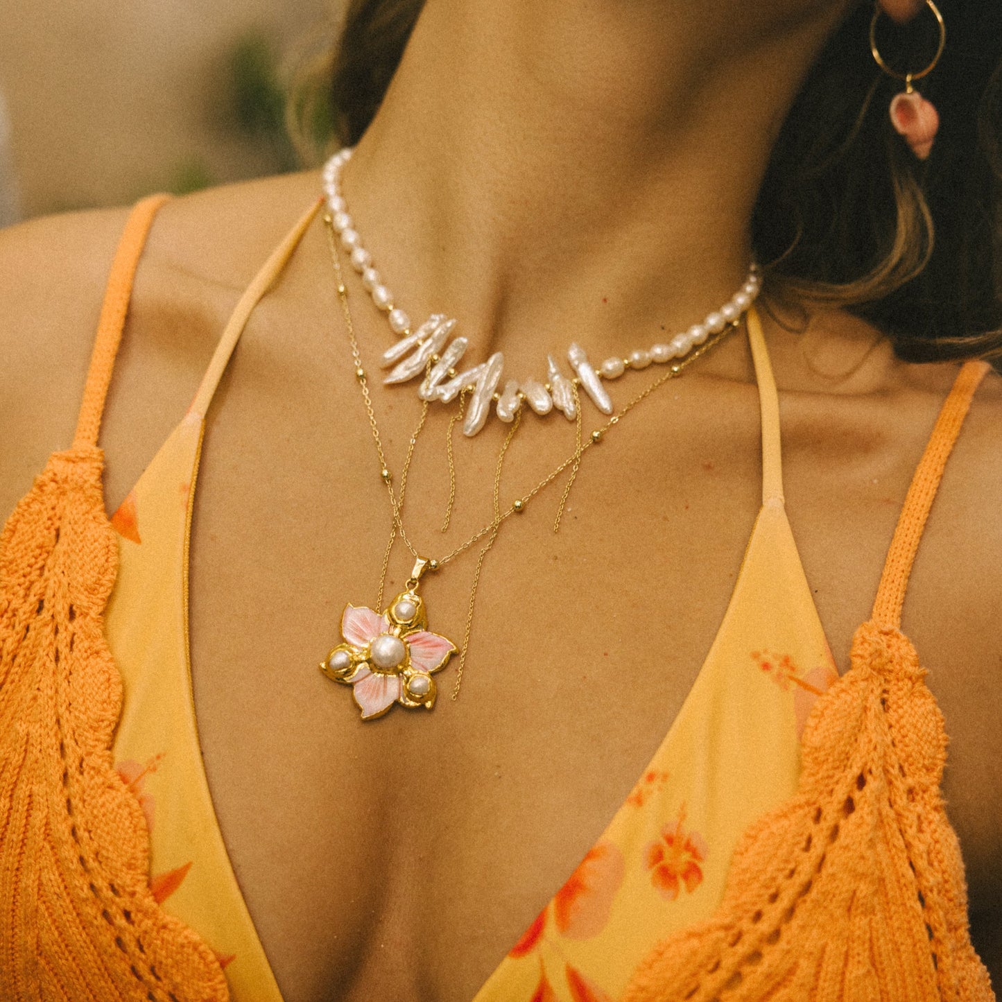 Close-up of a person wearing an orange top and pearl necklace with a pink flower pendant.