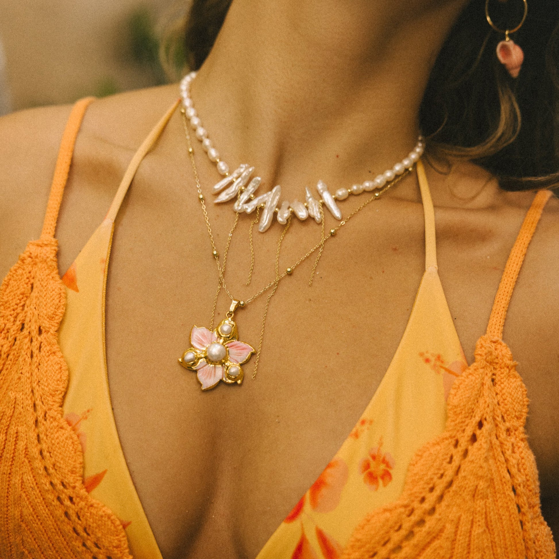 Close-up of a person wearing an orange top and pearl necklace with a pink flower pendant.