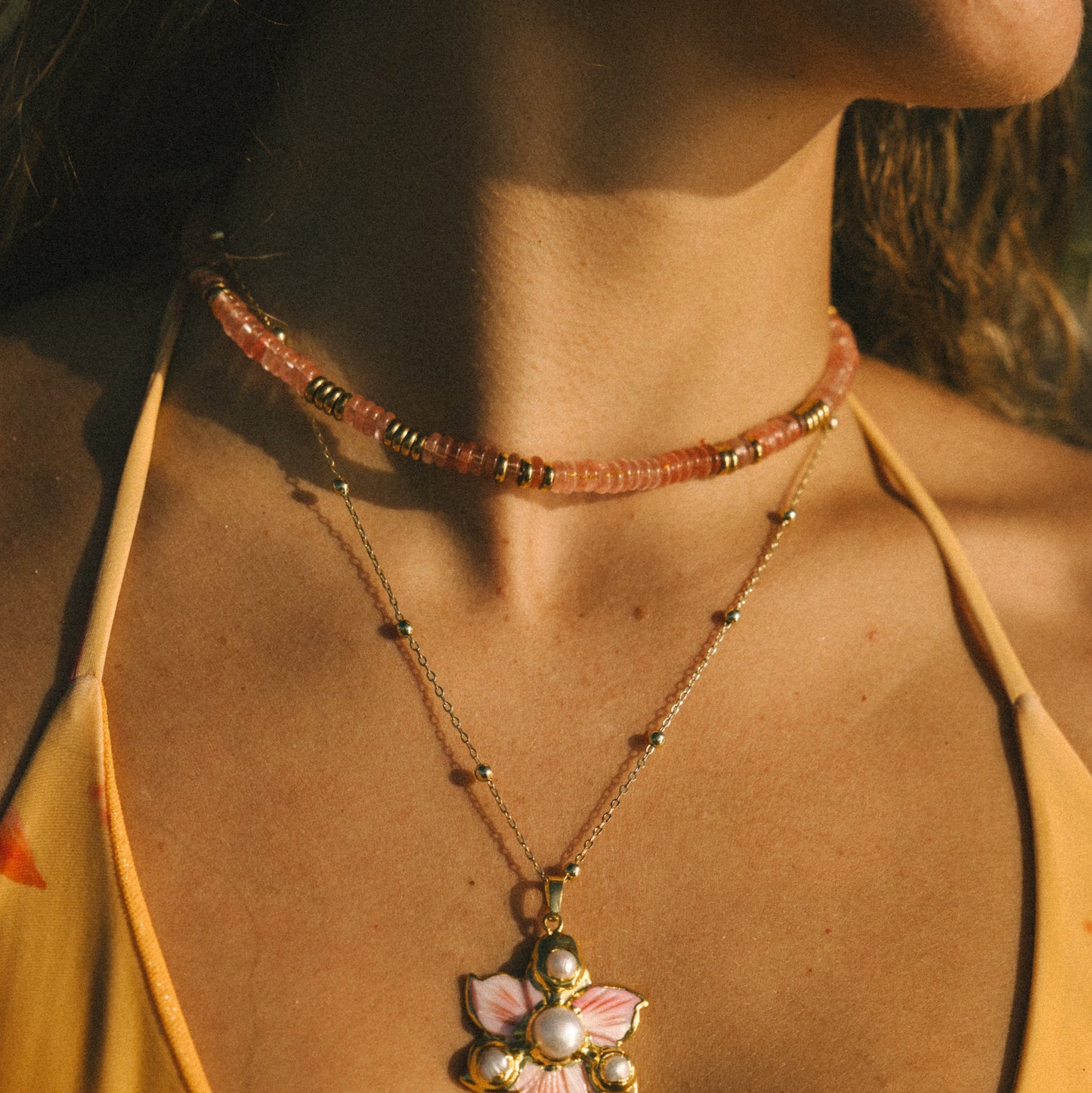 Close-up of a necklace with a floral pendant worn by a person in a yellow top.
