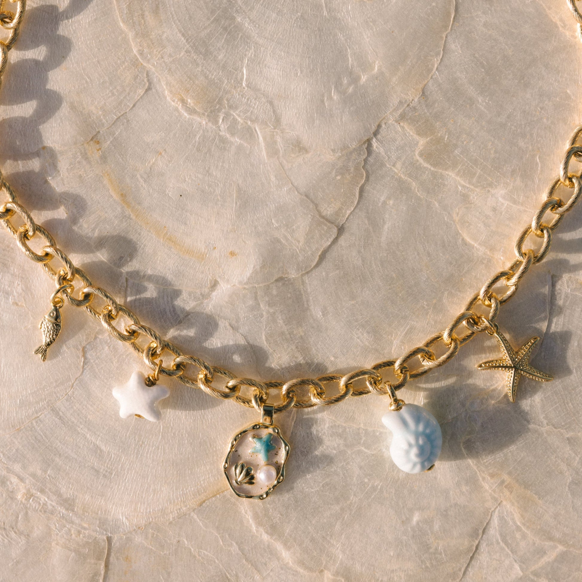 Gold chain bracelet with starfish and shell charms on a marble surface