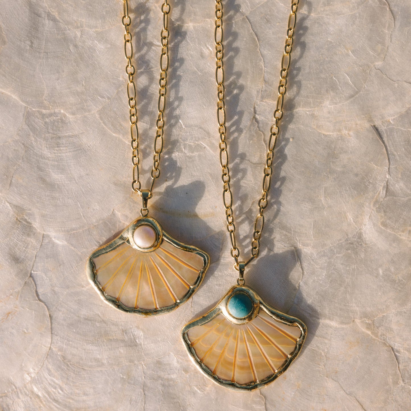 Two gold necklaces with shell-shaped pendants on a textured stone surface