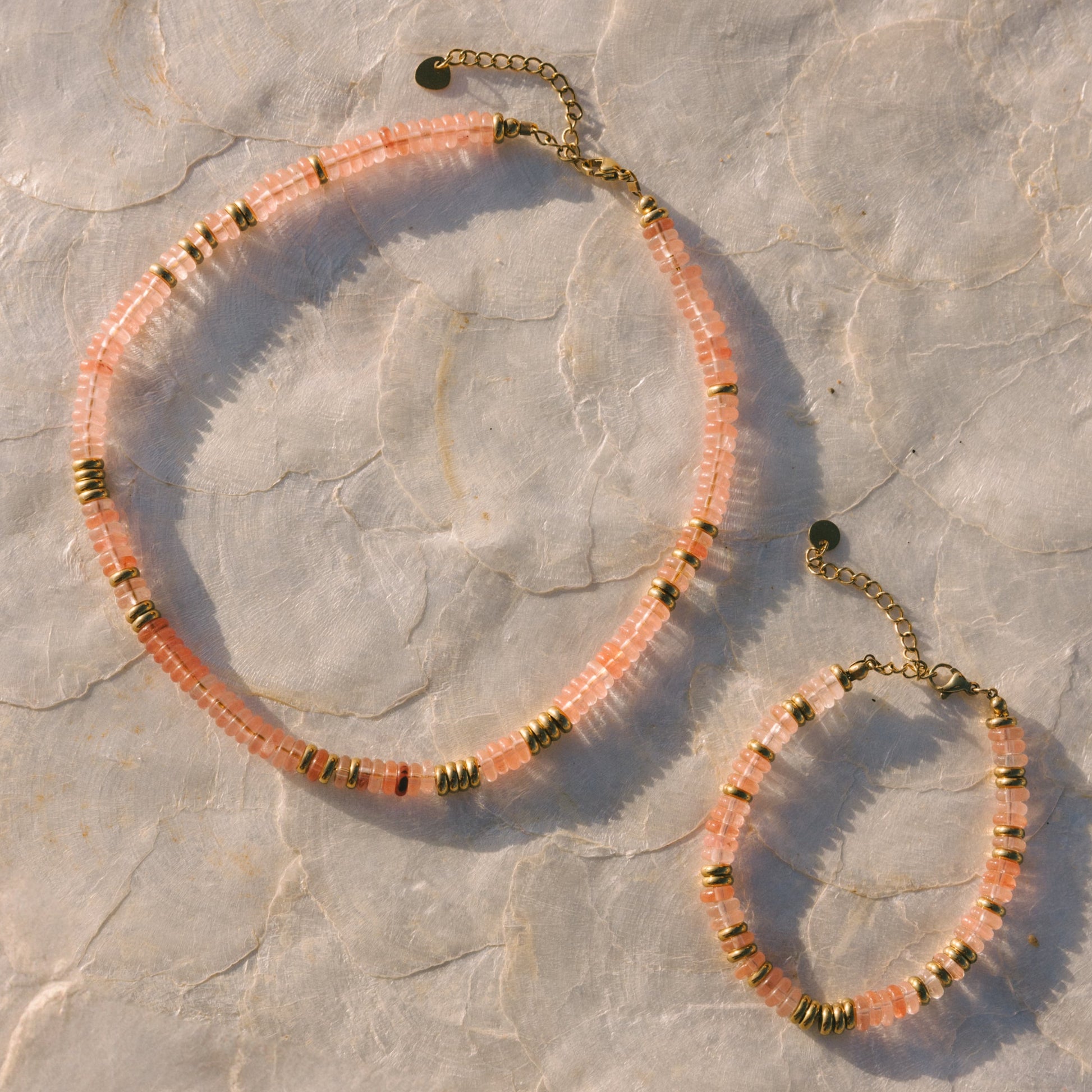 Necklace and bracelet set with pink and gold beads on a stone surface