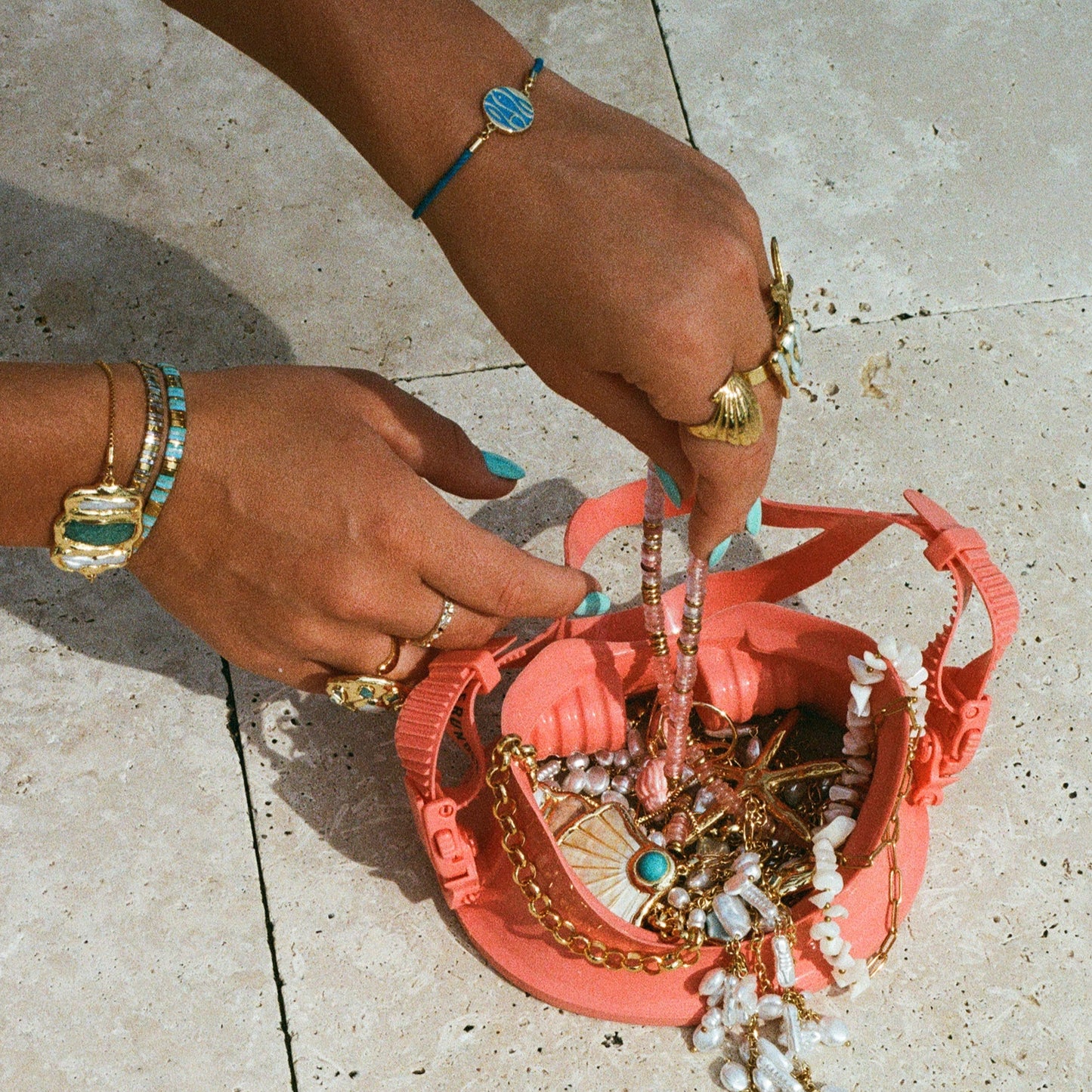 Person organizing jewelry in a pink bag on a light stone pavement.