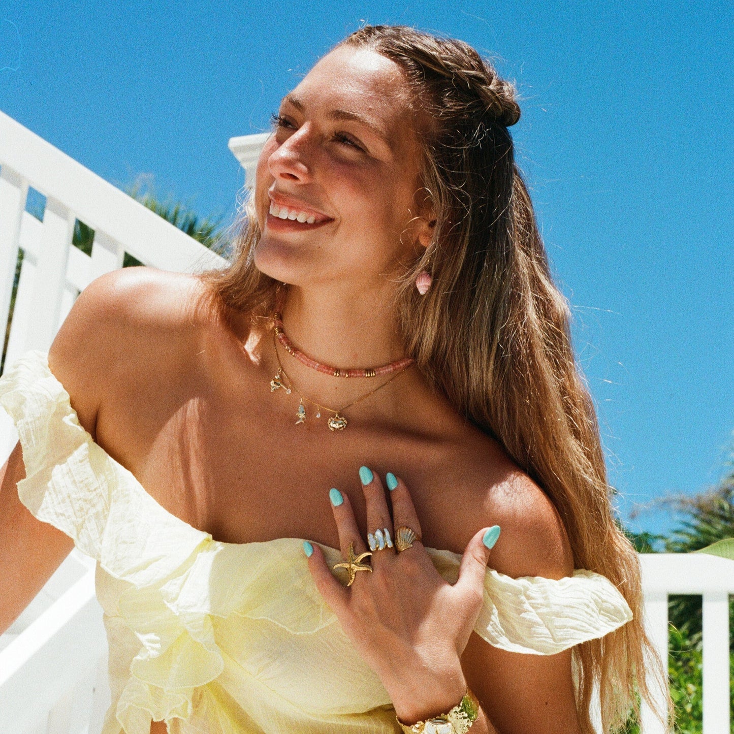 Woman in a yellow off-shoulder top standing on a balcony with a clear blue sky.