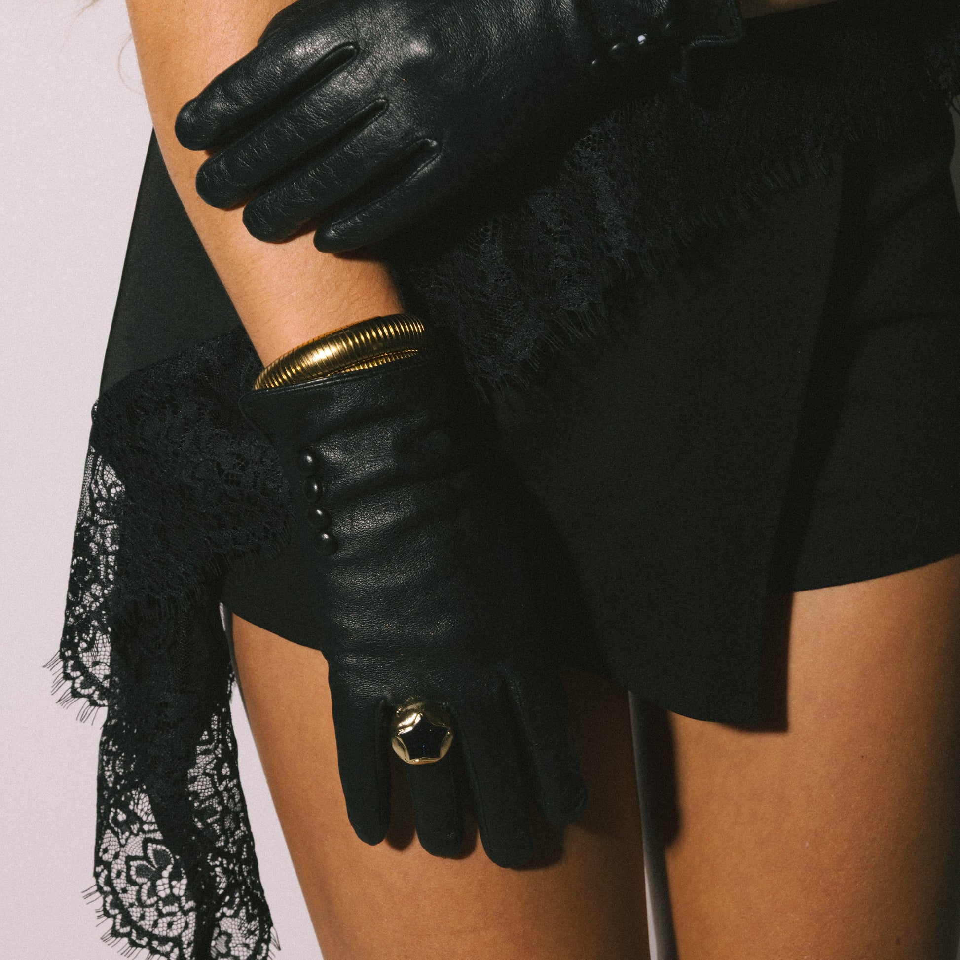 Person wearing black leather gloves with gold accents on a plain background