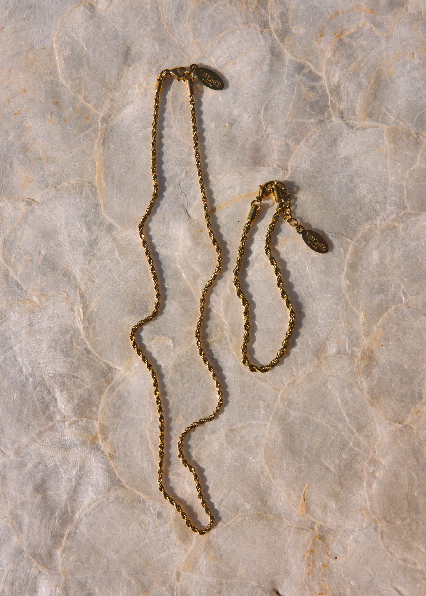 A vintage gold-toned chain necklace with a small oval pendant, displayed on a textured beige marble surface.