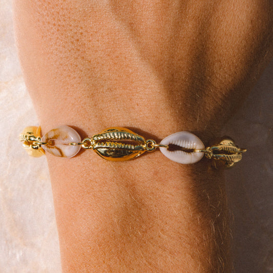 A close-up of a gold-toned bracelet with cowrie shells worn on a person's wrist.