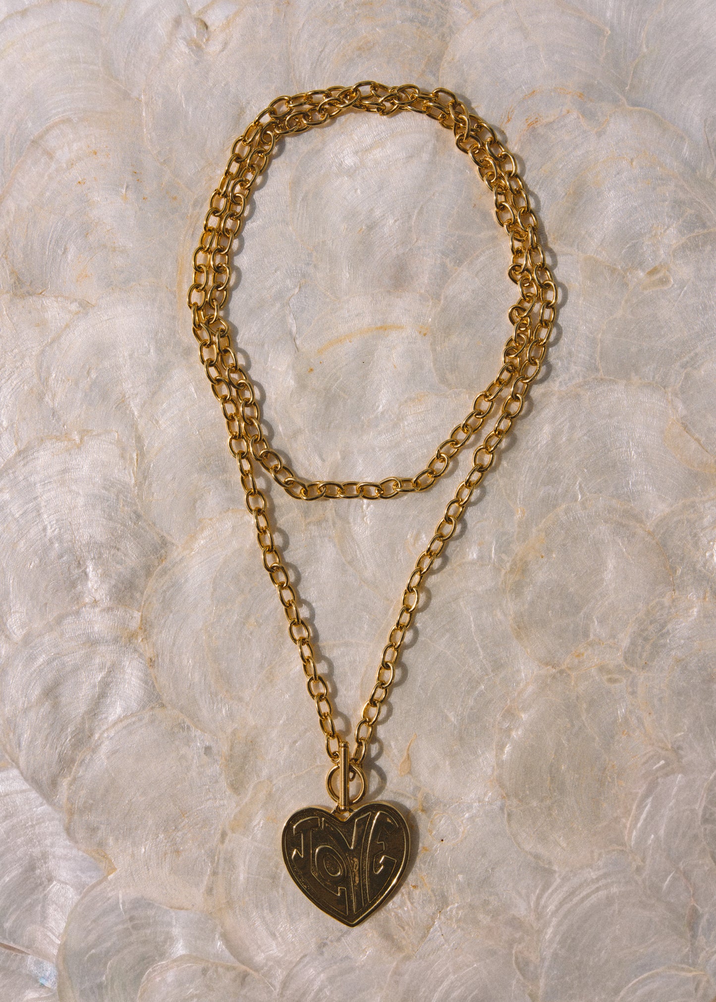 A gold-toned double-strand chain necklace with a heart-shaped pendant featuring engraved initials.