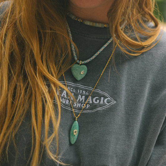 Person wearing a gray t-shirt with a visible brand logo, surrounded by greenery.