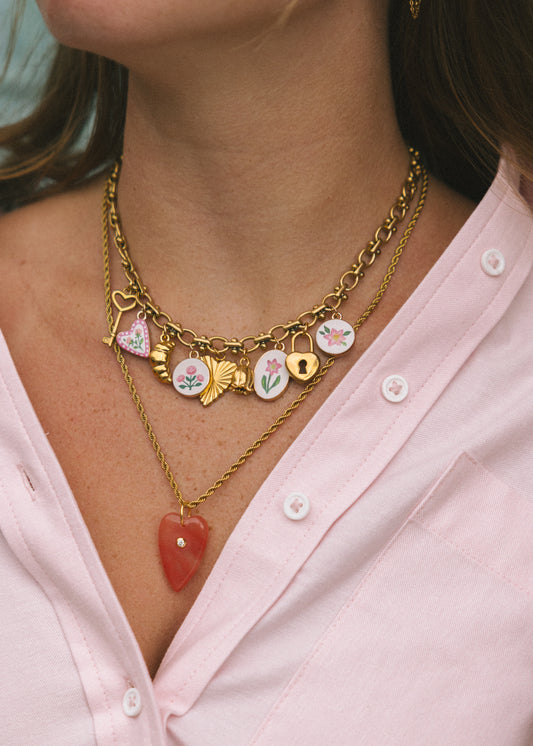 Close-up of a person wearing a gold necklace with heart-shaped and floral charms on a pink shirt.