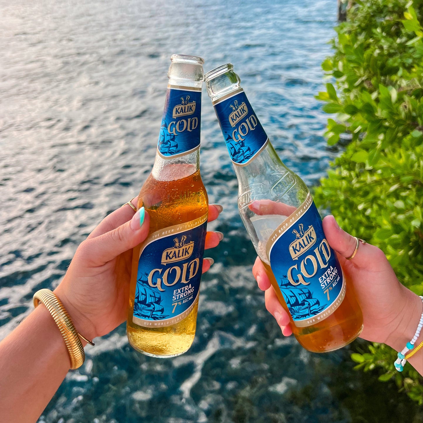 Two hands holding Kaldan Gold bottles by a waterfront
