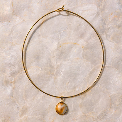 A delicate gold wire hoop necklace with a small oval pendant featuring a brown and cream marbled pattern, displayed on a light beige marble surface.