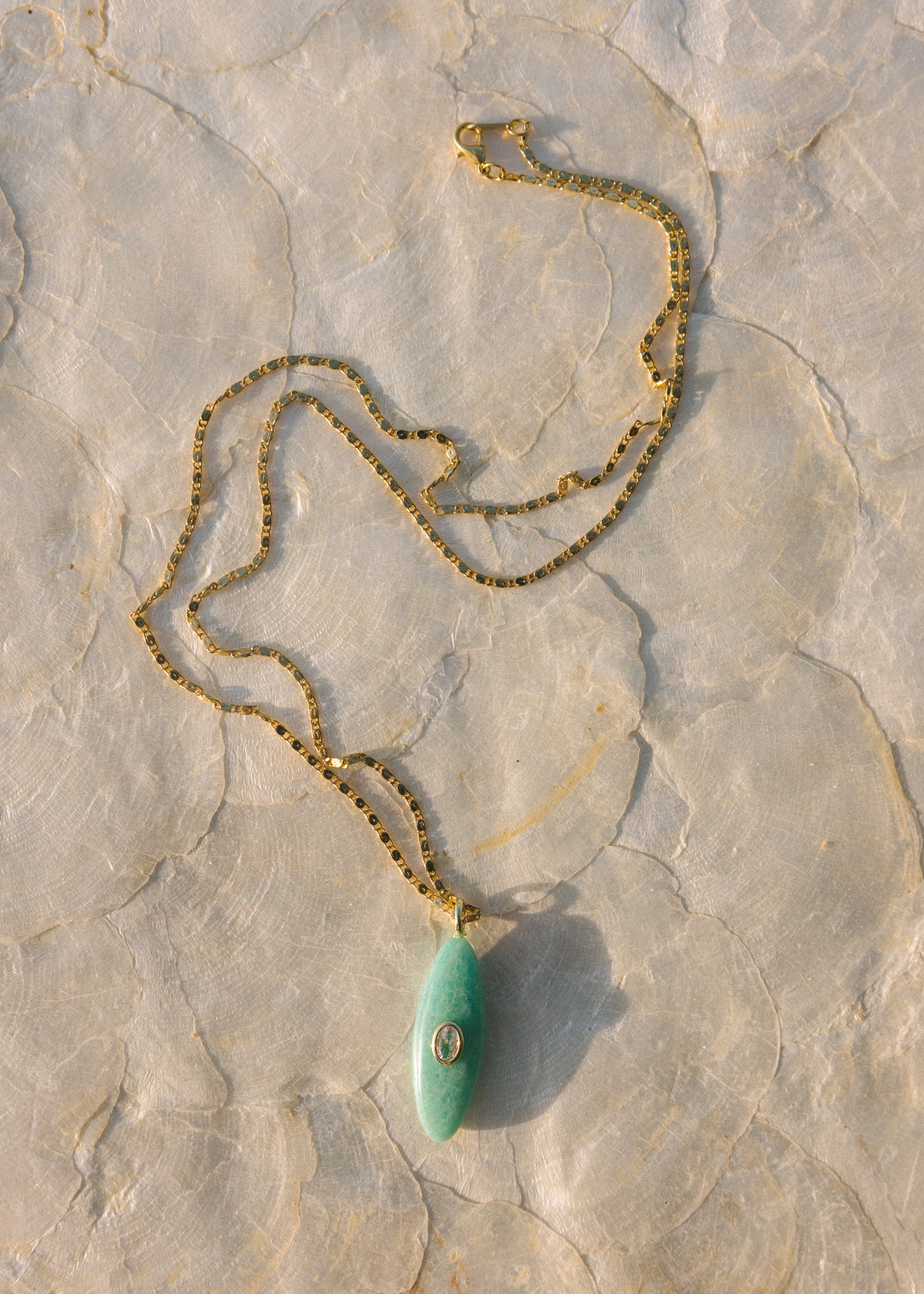 Gold necklace with a green pendant on a stone surface