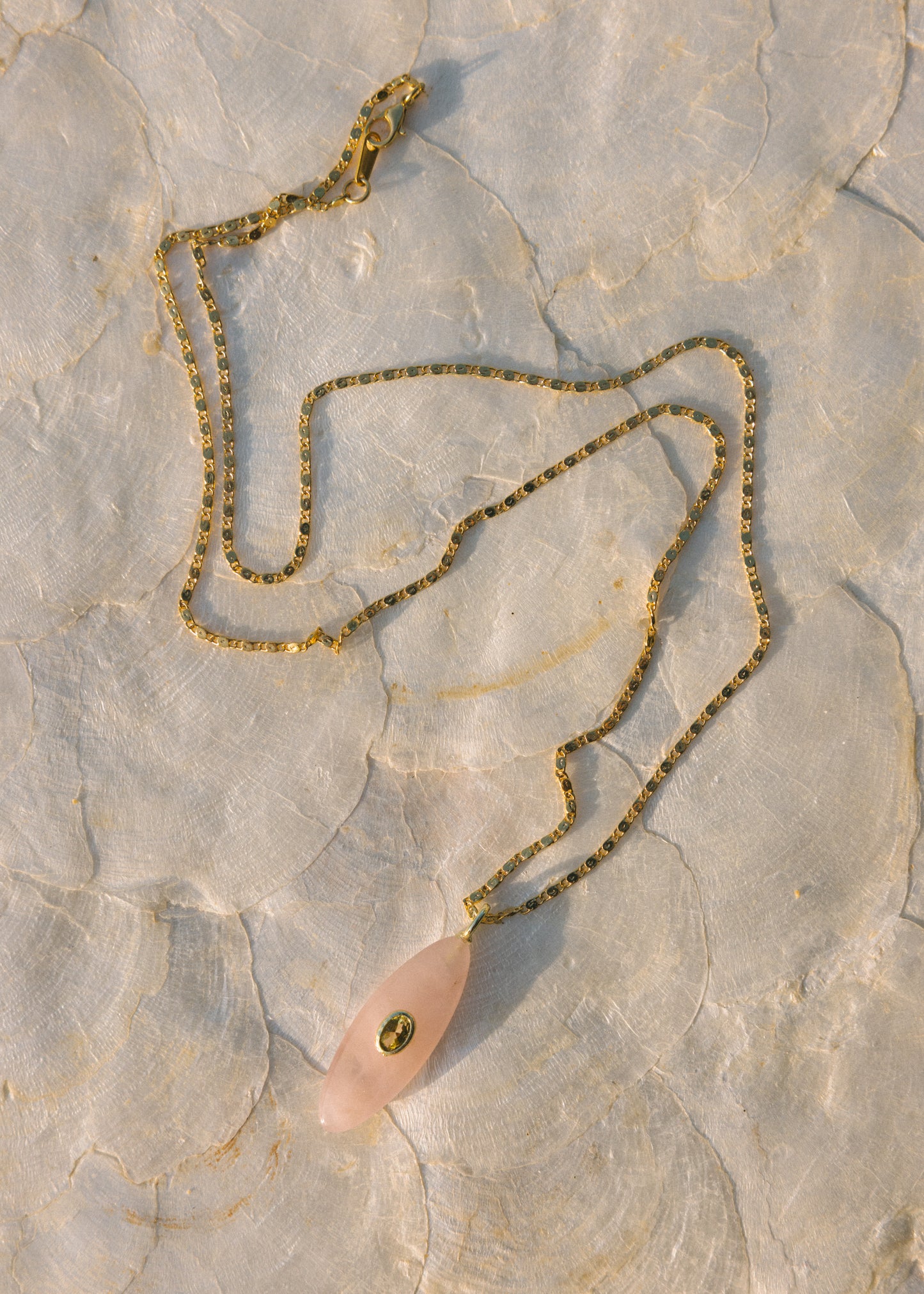 Necklace with a pink pendant and gold chain on a textured stone surface