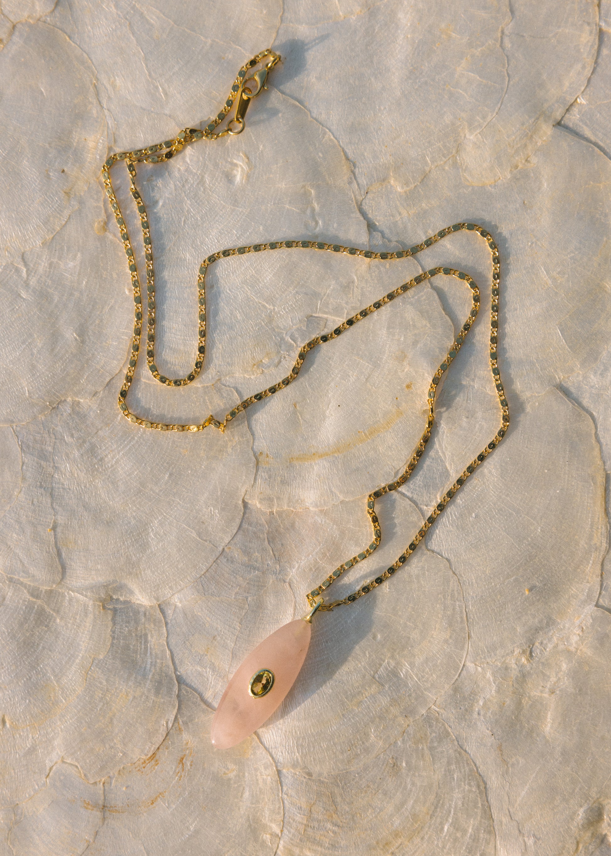 Necklace with a pink pendant and gold chain on a textured stone surface