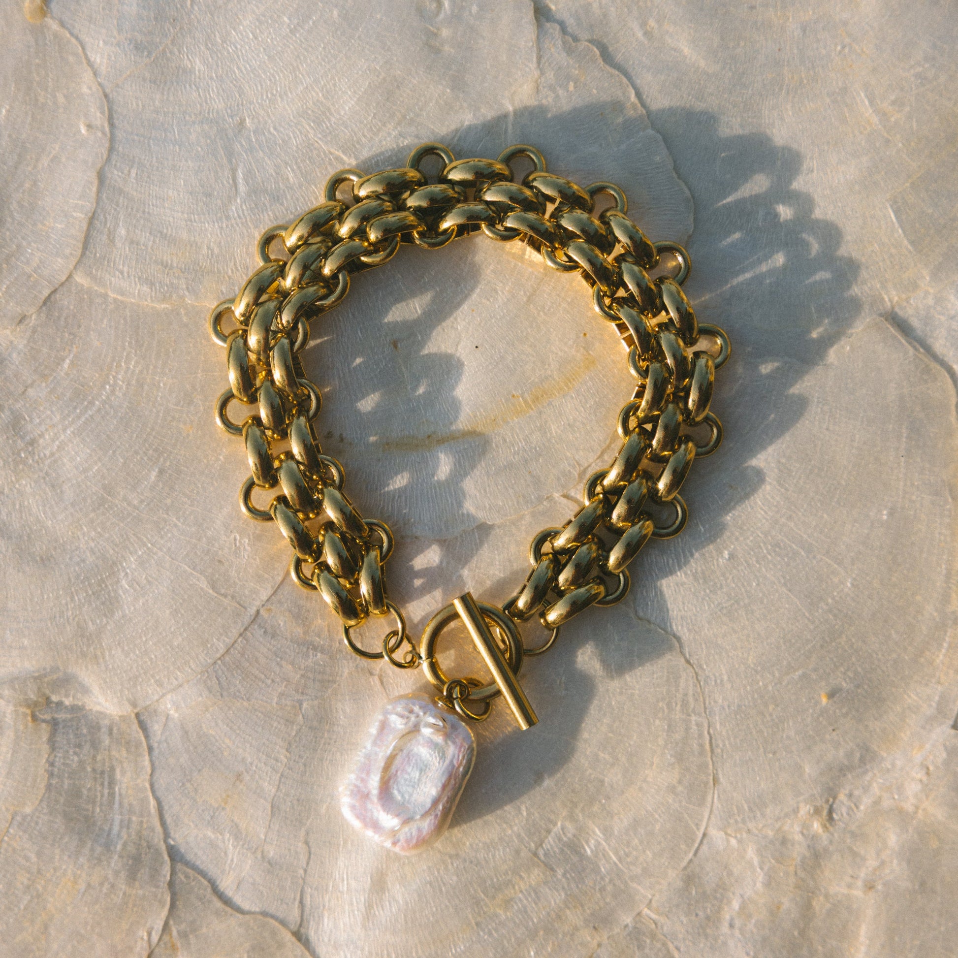 Gold chain bracelet with a pearl charm on a stone surface
