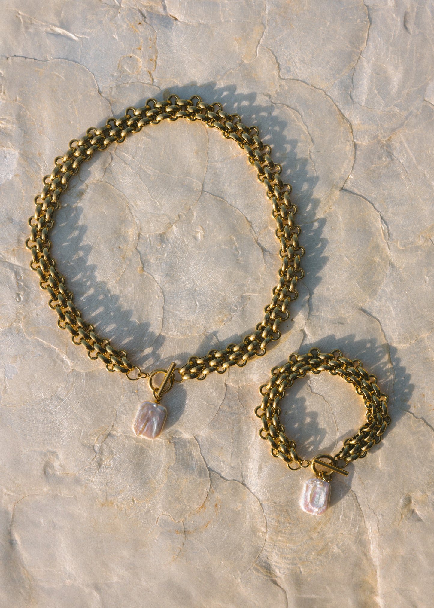 Gold chain bracelet with a heart-shaped charm on a stone surface