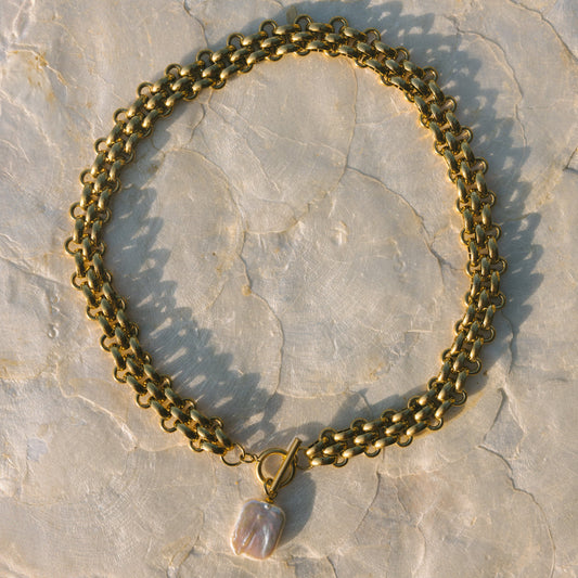 Gold chain necklace with a pendant on a stone surface