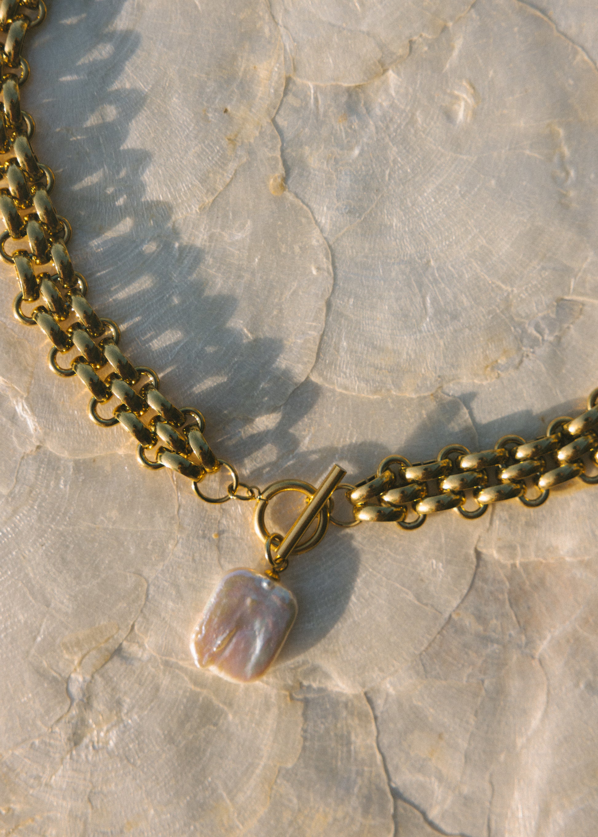 Gold chain necklace with a pearl pendant on a textured stone surface