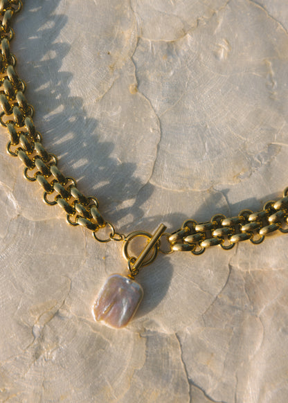Gold chain necklace with a pearl pendant on a textured stone surface