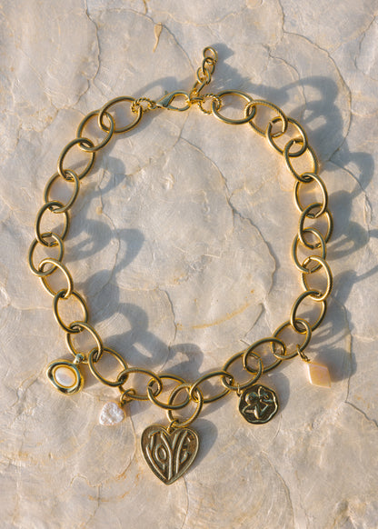Gold chain bracelet with heart and round charms on a stone surface