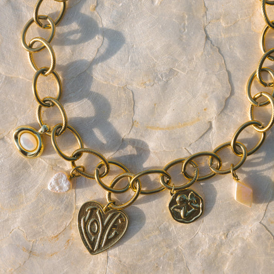 Gold chain necklace with heart-shaped charm on a textured stone surface