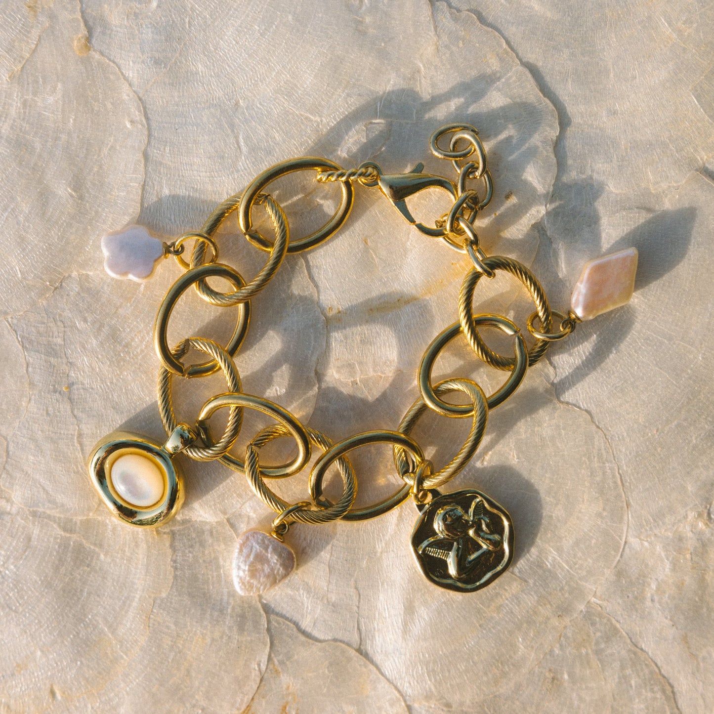 Gold chain bracelet with charms on a stone surface