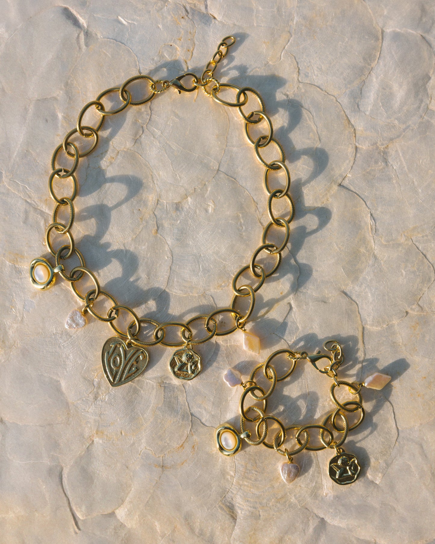 Gold chain bracelet with heart and paw print charms on a textured stone surface