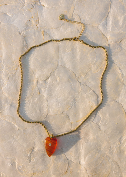 Gold necklace with a red pendant on a textured stone surface