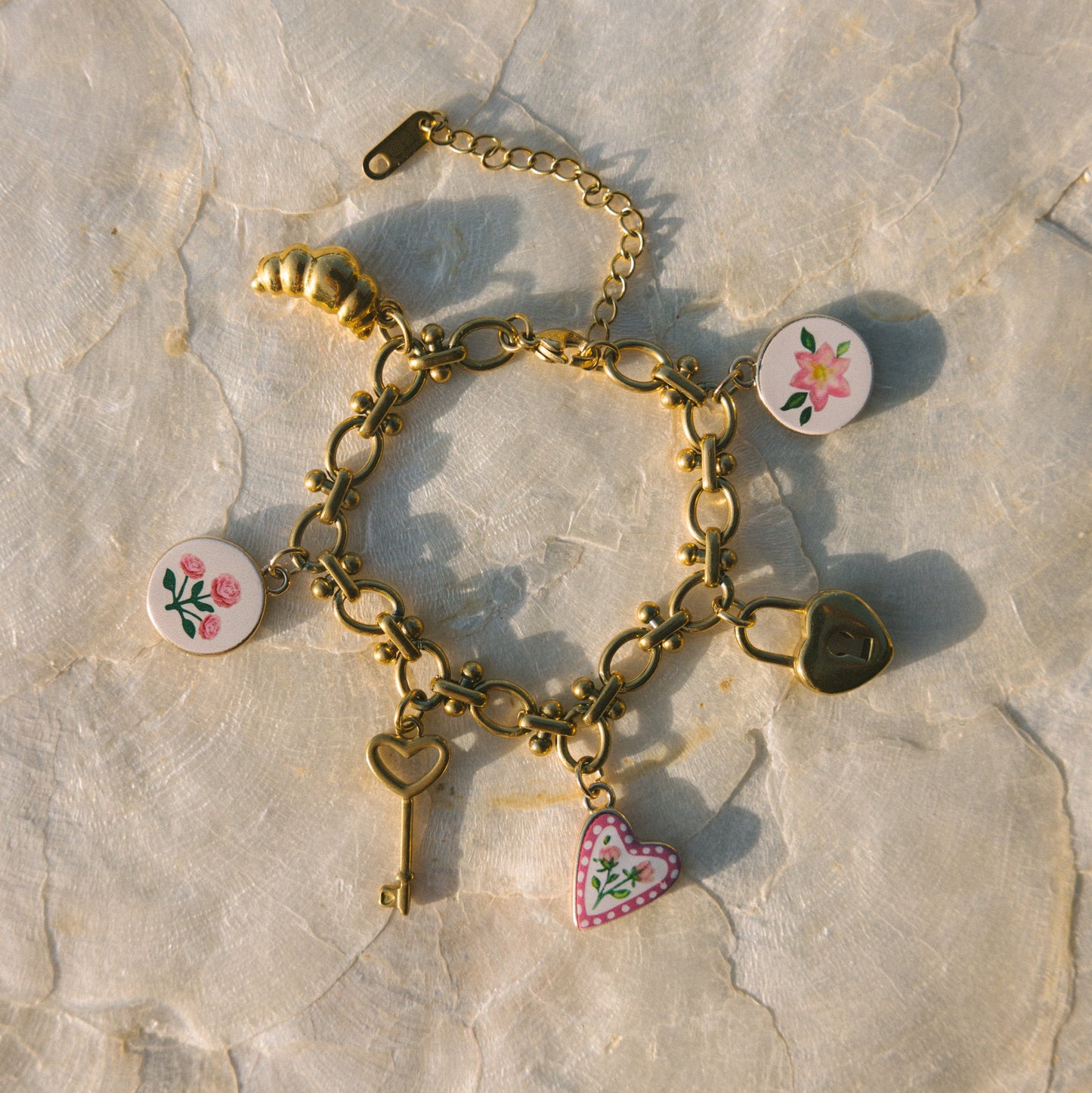 Gold bracelet with heart and floral charms on a stone surface