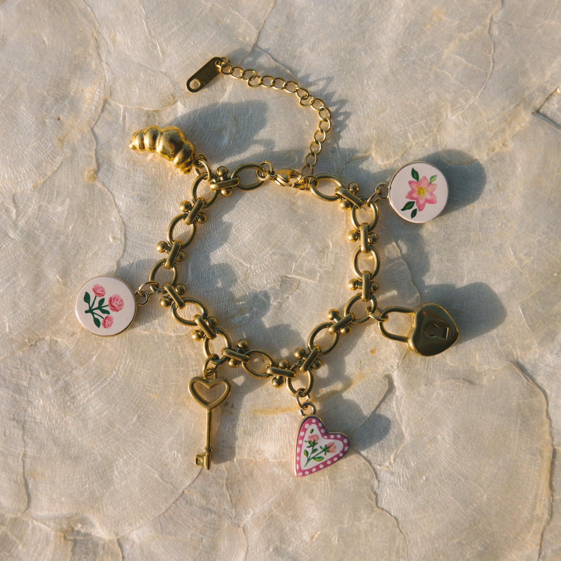 Gold bracelet with heart and floral charms on a stone surface