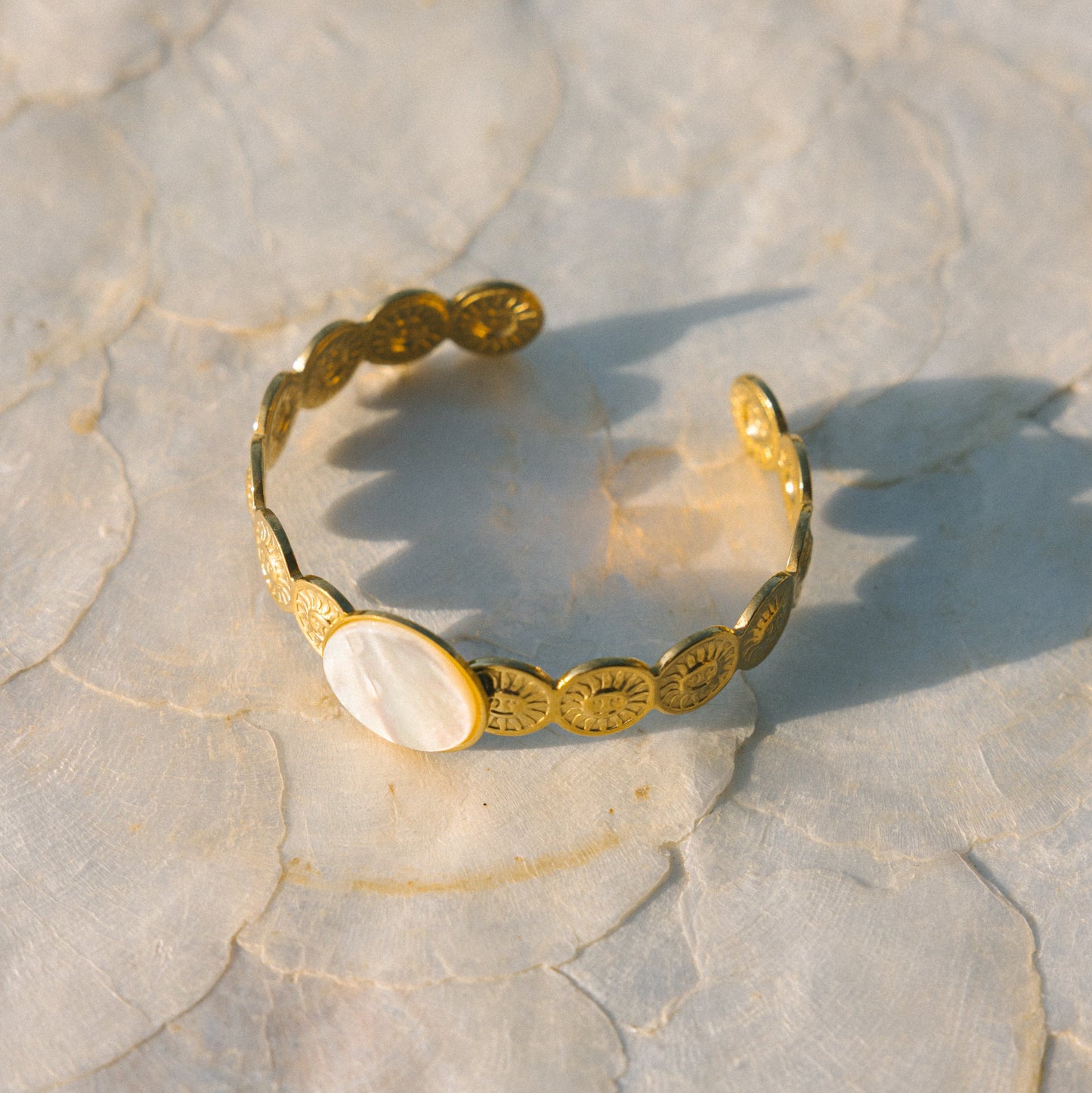 Gold bracelet with shell elements on a textured stone surface