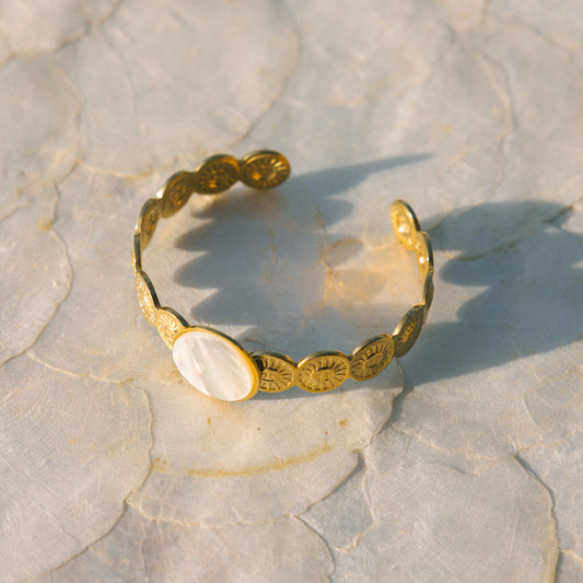 Gold bracelet with shell elements on a textured stone surface